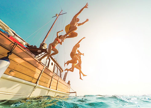 Jóvenes saltando dentro de océano en el día de la excursión de verano - amigos felizes buceo de barco de vela en el concepto de juventud y la diversión del Mar - vacaciones, distorsión de la lente ojo de pez - foco en silueta de cuerpos- photo