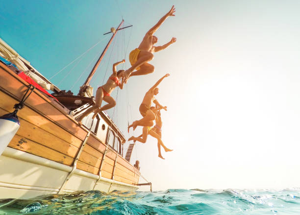 giovani che saltano all'interno dell'oceano nel giorno delle escursioni estive - amici felici che si tuffano dalla barca a vela al mare - concetto di vacanza, gioventù e divertimento - focus sulla silhouette dei corpi - distorsione dell'obiettivo fisheye - tropical climate water leisure activity holidays foto e immagini stock