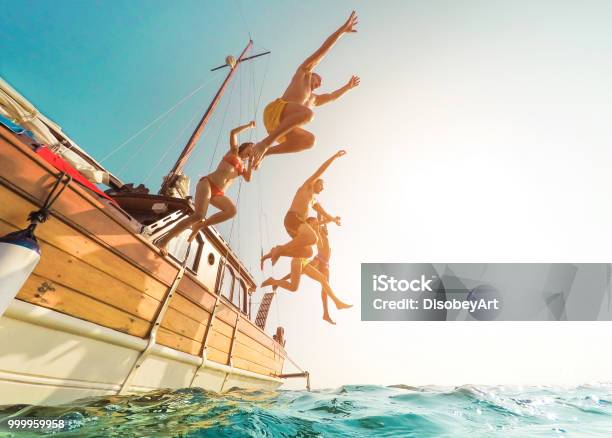 Young People Jumping Inside Ocean In Summer Excursion Day Happy Friends Diving From Sailing Boat Into The Sea Vacation Youth And Fun Concept Focus On Bodies Silhouette Fisheye Lens Distortion Stock Photo - Download Image Now
