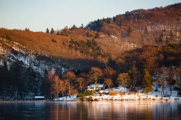 Evening view over the frozen Obersee of lake Rursee with a house by the shore in winter in the Eifel, Germany.