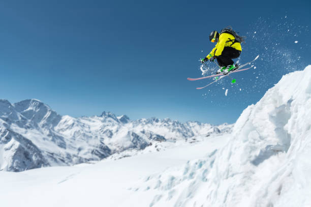 A skier in full sports equipment jumps into the precipice from the top of the glacier against the background of the blue sky and the Caucasian snow-capped mountains. Elbrus region. Russia stock photo