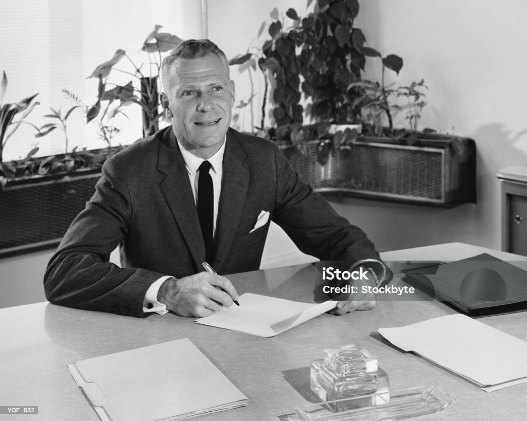 Man sitting at desk, holding paper and pencil  Black And White Stock Photo