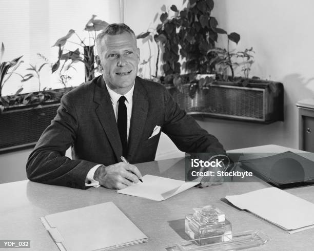 Man Sitting At Desk Holding Paper And Pencil Stock Photo - Download Image Now - Black And White, The Past, White People