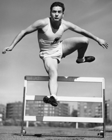In a jump. Hurdler. Young man professional track athlete, running training isolated over black background. Speed and strength. Concept of sport, action, energy, health, movement. Copy space for ad