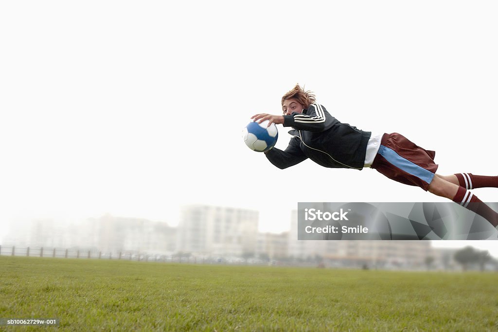 Teenage boy (14-15) diving to catch football - Photo de Gardien de but libre de droits