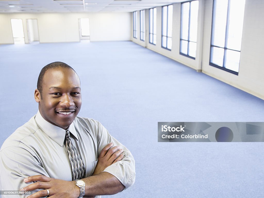 Businessman standing in empty office with arms crossed, smiling, portrait  Businessman Stock Photo