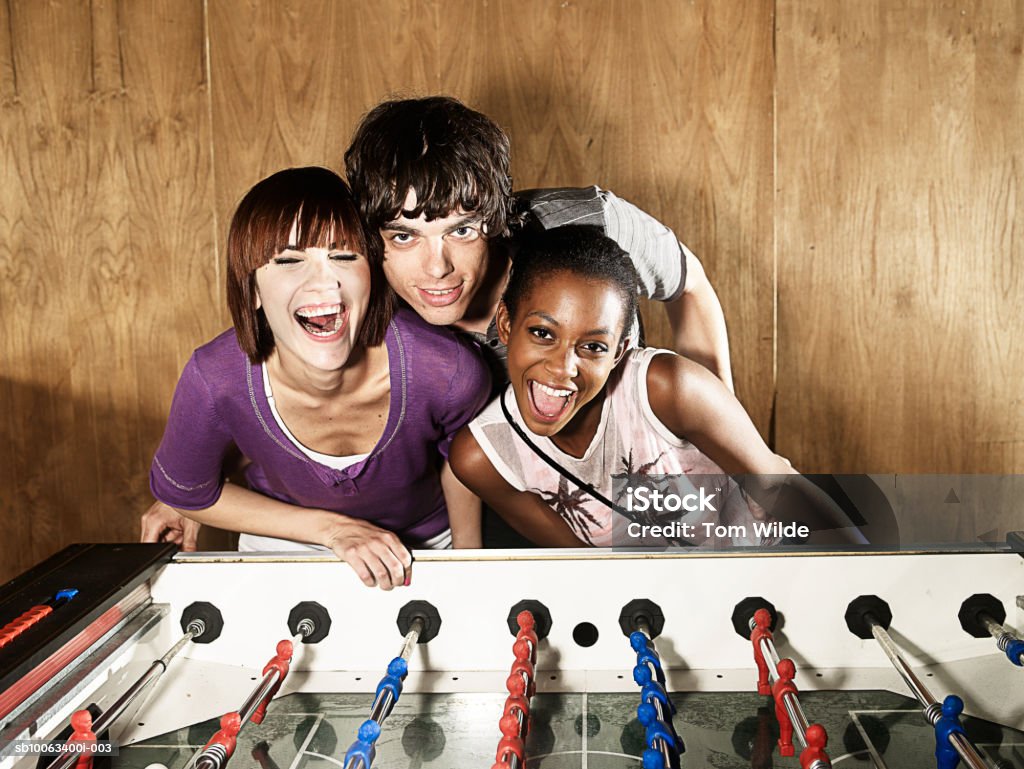 Young man standing with two women by table football game, portrait - Foto de stock de Gritar libre de derechos