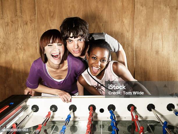 Young Man Standing With Two Women By Table Football Game Portrait Foto de stock y más banco de imágenes de Gritar