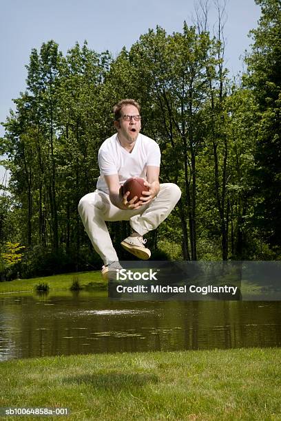 Photo libre de droit de Man Jumping To Catch Rugby Ball In Front Of Lake Mouth Open banque d'images et plus d'images libres de droit de Rugby - Sport