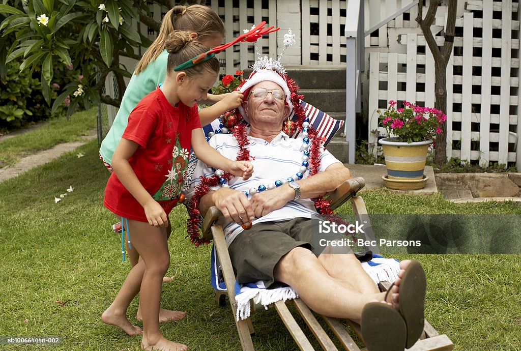 Children (7-9) decorating senior man with Christmas decorations in yard  Christmas Stock Photo