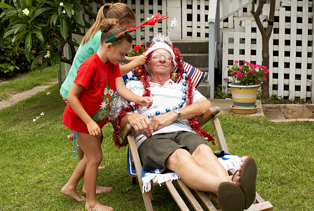 Children (7-9) decorating senior man with Christmas decorations in yard  man sleeping chair stock pictures, royalty-free photos & images