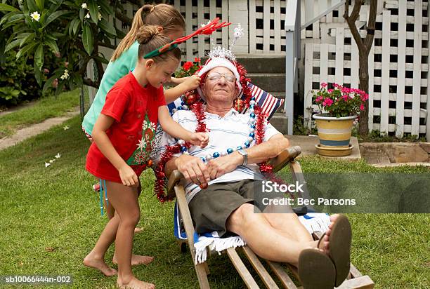 Children Decorating Senior Man With Christmas Decorations In Yard Stock Photo - Download Image Now