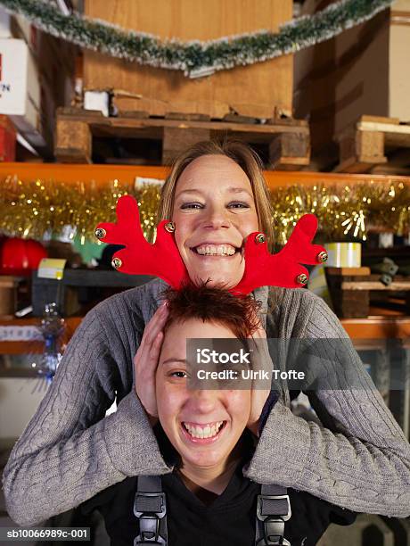 Young Woman Holding Christmas Reindeer Antlers On Other Womens Head Portrait Stock Photo - Download Image Now
