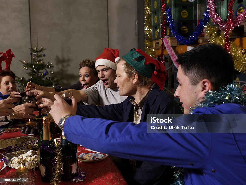 Group of workers sitting at christmas table in warehouse toasting with wine glasses  Christmas Stock Photo