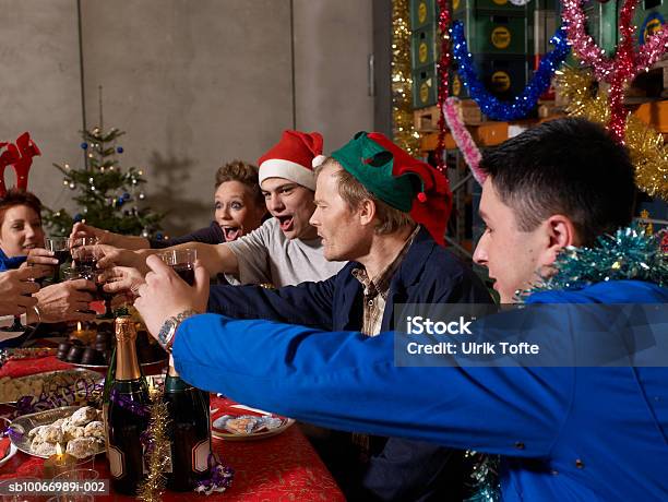 Group Of Workers Sitting At Christmas Table In Warehouse Toasting With Wine Glasses Stock Photo - Download Image Now
