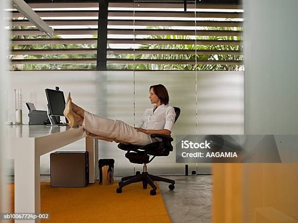 Photo libre de droit de Businesswoman With Feet Up On Desk banque d'images et plus d'images libres de droit de 55-59 ans - 55-59 ans, Adulte, Adulte d'âge mûr