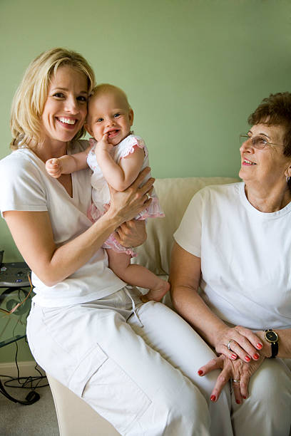 grandmother, mother and baby girl (9 months) on sofa - grandmother senior adult child baby - fotografias e filmes do acervo