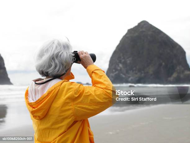 Senior Woman Looking Through Binoculars On Beach Stock Photo - Download Image Now - Binoculars, One Woman Only, Looking Through An Object