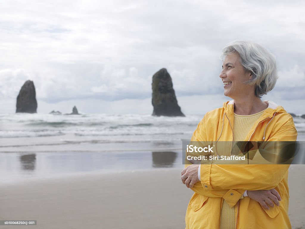 Sênior Mulher na praia com braços cruzados e sorrindo - Foto de stock de Terceira idade royalty-free