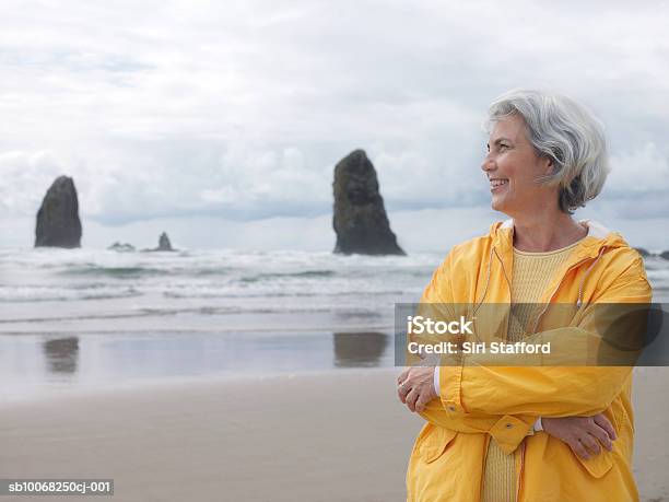 Mulher Idosa Na Praia Com Os Braços Cruzados A Sorrir - Fotografias de stock e mais imagens de Terceira idade