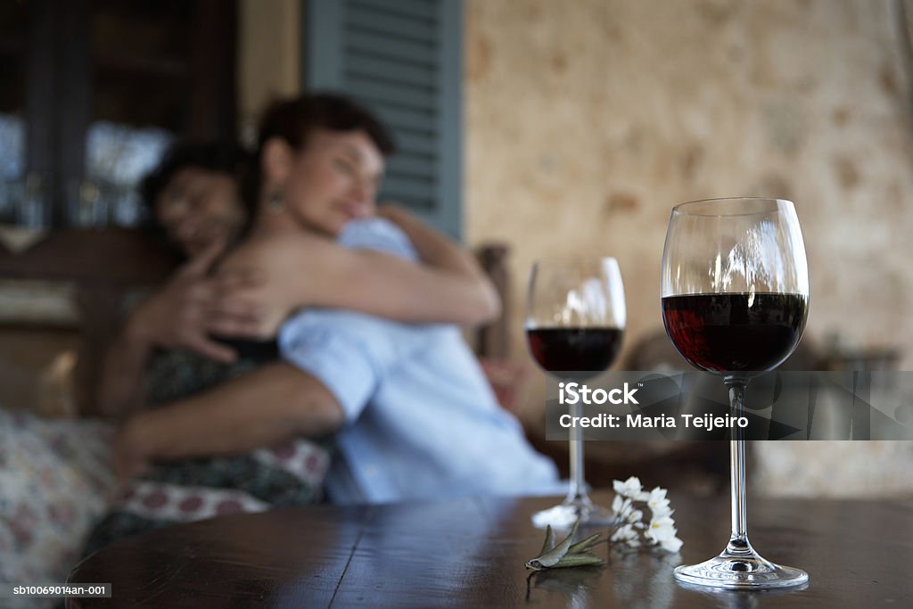 Couple cuddling on porch, focus on wineglasses in foreground  35-39 Years Stock Photo