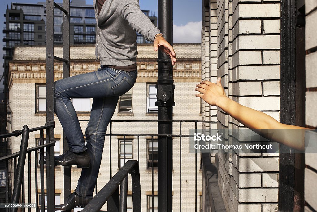 Man climbing ladder in balcony, stretching hand for woman  Reaching Stock Photo