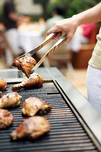 woman holding barbecuing chicken on grill with tongs, close-up - rf ストックフォトと画像