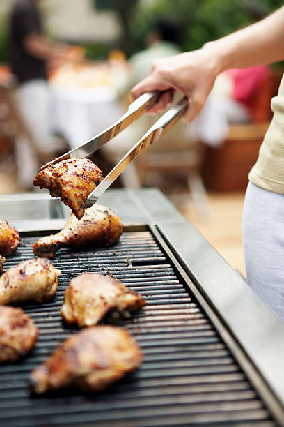 woman holding barbecuing chicken on grill with tongs, close-up - food tong 뉴스 사진 이미지