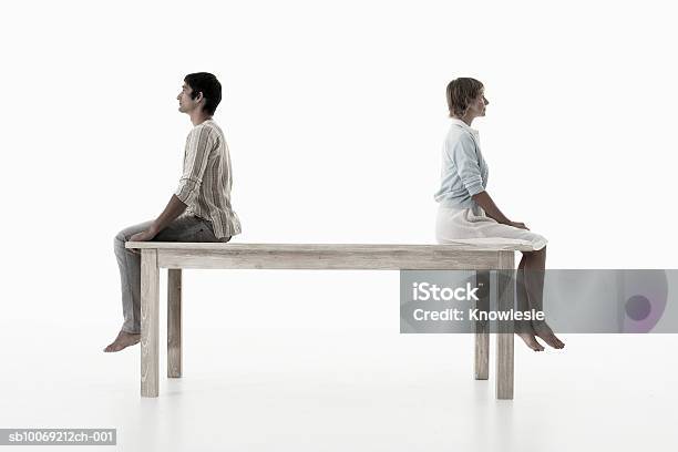 Couple Sitting Back To Back On Wooden Table Against White Background Side View Stockfoto en meer beelden van Aan de kant van