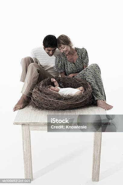 Couple Looking At Baby Girl Lying In Birds Nest On Wooden Table Against White Background Stock Photo - Download Image Now