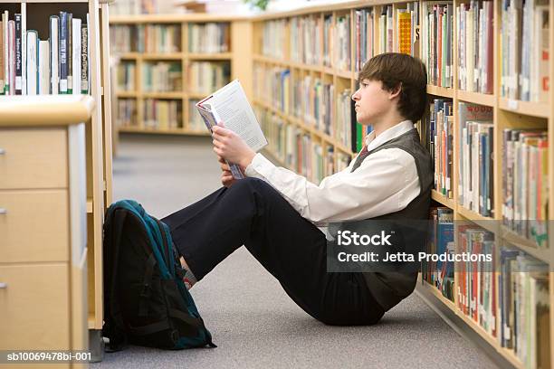 Schule Junge Liest Auf Etage Mit Bücherregal In Bibliothek Stockfoto und mehr Bilder von Bibliothek