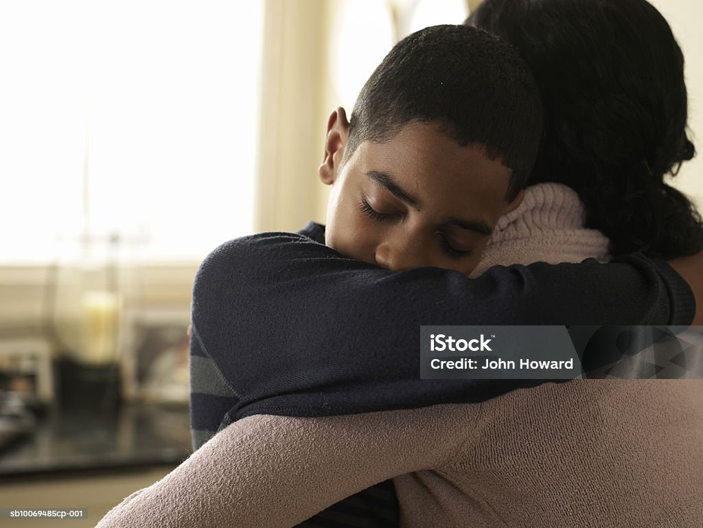 Boy (12-13) hugging mother at home  Embracing Stock Photo