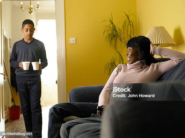 Boy Carrying Two Mugs Mother Sitting On Sofa Stock Photo - Download Image Now
