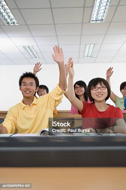 University Students Raising Hands In Classroom Smiling Stock Photo - Download Image Now