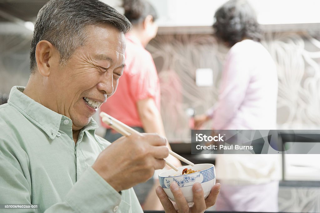 Senior man eating with chopsticks, women in background - Lizenzfrei 40-44 Jahre Stock-Foto