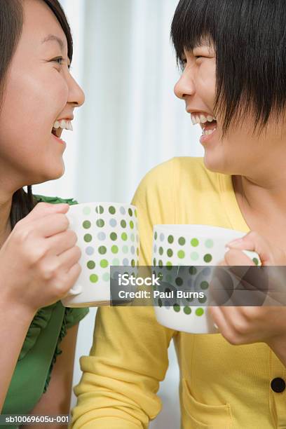 Teenage Girl And Young Woman Holding Coffee Mugs Laughing Foto de stock y más banco de imágenes de 16-17 años