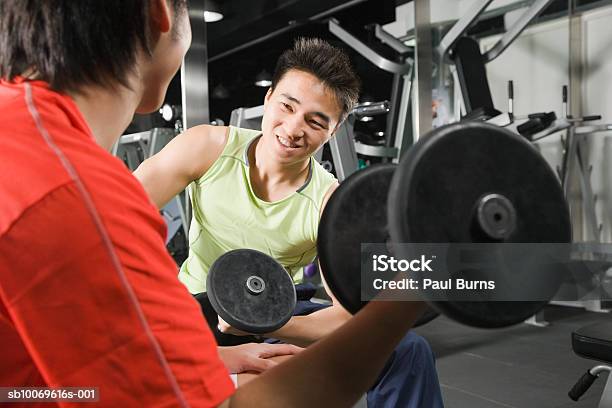 Two Young Men Exercising With Dumbbells In Gym Smiling Stock Photo - Download Image Now