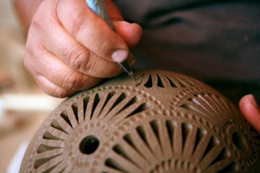Top view closeup of female artisan decorating handmade ceramics with plant imprint using immortelle flower, copy space