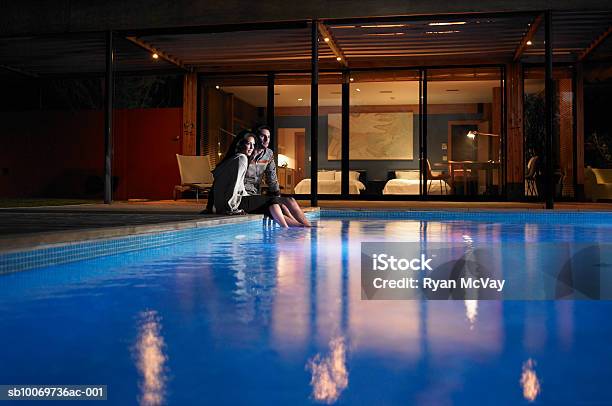 Young Couple Sitting At Edge Of Pool At Night Stock Photo - Download Image Now - Swimming Pool, Night, Hotel