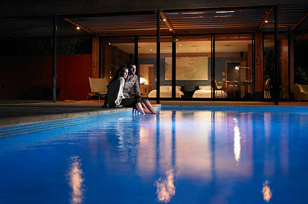 casal jovem sentado à beira da piscina à noite - ankle deep in water imagens e fotografias de stock