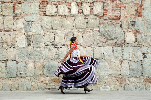 Mexico, Oaxaca, Istmo, young woman in traditional dress walking by stone wall photo