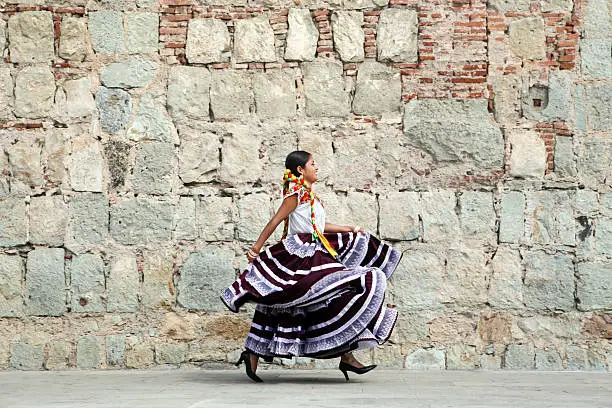 Photo of Mexico, Oaxaca, Istmo, young woman in traditional dress walking by stone wall