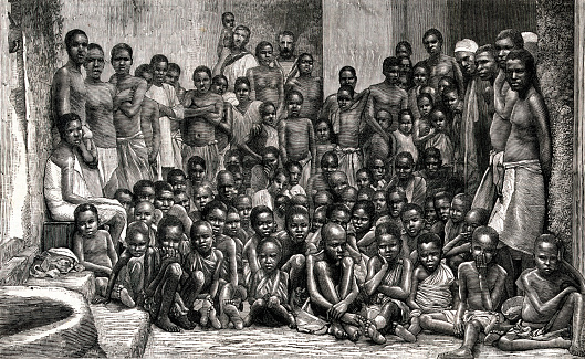 Vintage engraving shows a crowd of African men, women, and children who had been rescued by the British navy from a slaving vessel in 1884. Two British sailors from the HMS Undine are seen in the background. Although the slave trade was abolished in many countries during the 19th century, slave trading continued in other countries.