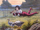 istock Antique illustration - Mother Goose 1887 - boy laying in meadow playing a flute with geese near by 1336101968