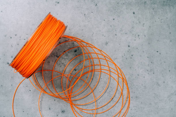 3d Printer Plastic Filament. Spool of orange  thermoplastic wire for 3D printing close up on grey stone background, flat lay stock photo