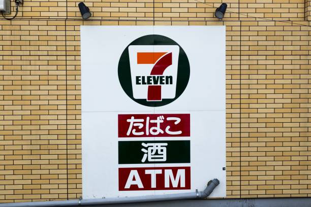 7-Eleven Store Sign with Japanese Translation in Tokyo Tokyo, Japan - February 7, 2020:  Convenience Store Sign against Yellow Brick Wall with Japanese letters that read “Seven Eleven” and “ATM” number 711 stock pictures, royalty-free photos & images