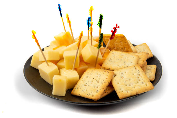 a black plate of whole wheat buicuits and cheddar cheese cube appetizers with fancy toothpicks isolated on white A tasty cheddar cheese and pepperoni appetizer plate for a party muenster cheese stock pictures, royalty-free photos & images