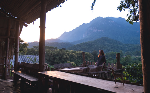 a female traveler standing on wooden balcony and looking at a beautiful mountains view