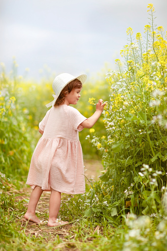 a girl in a hat on a rapeseed field is looking at flowers