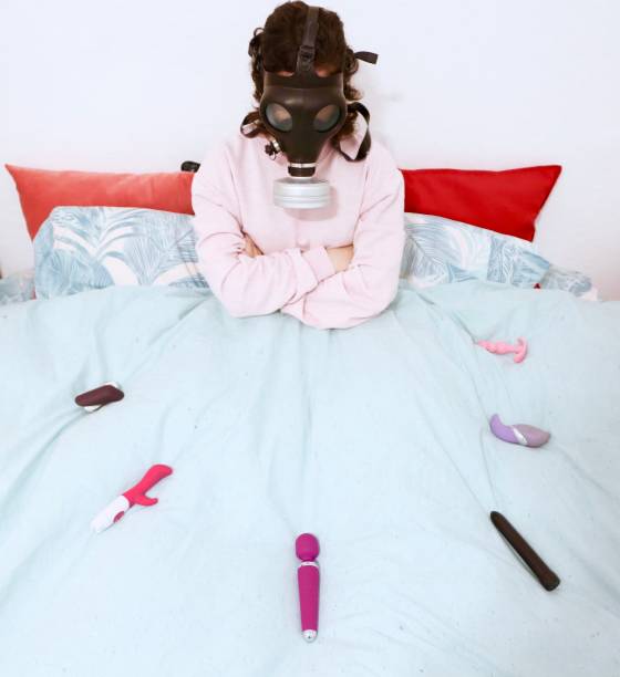 une fille dans le lit avec des jouets sexuels et le masque à gaz - gode photos et images de collection
